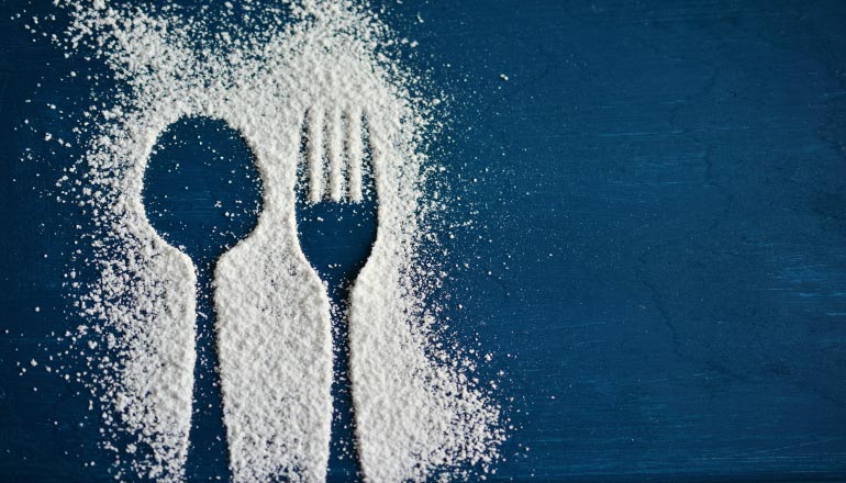 Aerial view of an outside of a spoon and fork in a dusting of sugar on a dark blue background